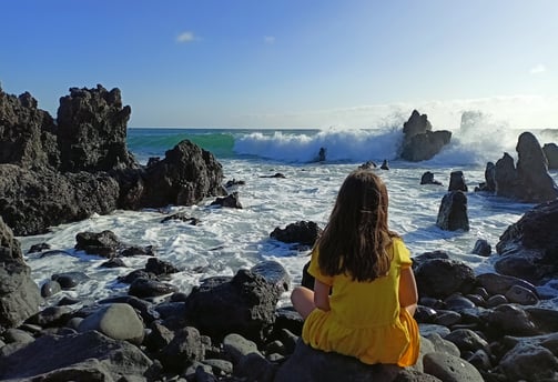 a little girl sitting on rocks before the ocean