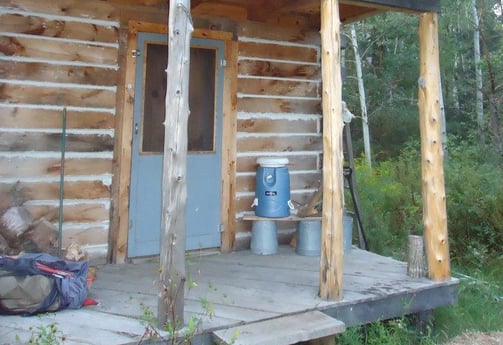 the porch of a rustic wood cabin, with a cooler for water resting on a makeshift shelf