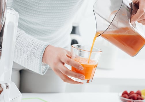 a person pouring a drink into a glass of juice