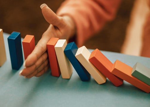 a women's hand stopping dominos from falling