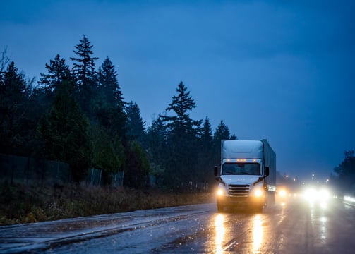 After-hours delivery truck driving at night on wet road — reliable freight service after hours.