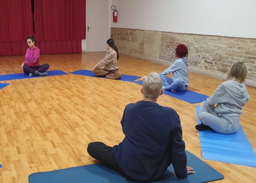 a group of people sitting on yoga mats in a circle, classe di esercizi di bioenergetica