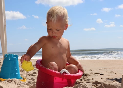photographer portrait of a baby in a pink bucketle on a beach
