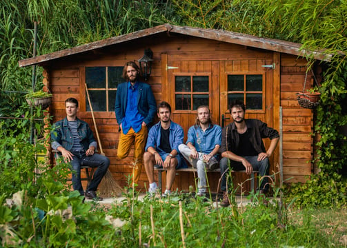 photographie d'un groupe de musiciens de rock devant un cabanon de jardin en pleine nature