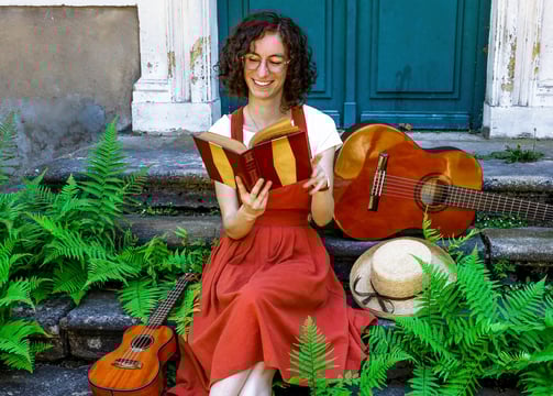 musicienne en train de lire un livre/a woman in a red dress reading on stairs with guitar beside her
