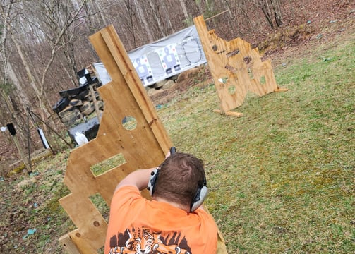 Kneeling man engaging targets from a barrier using self-defense firearm during training.