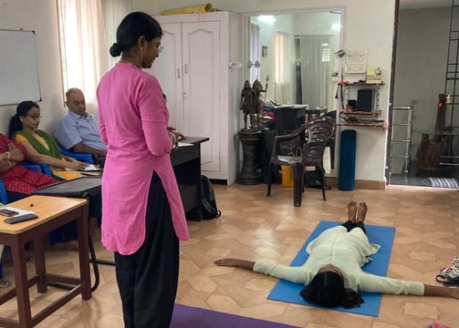 a woman in a pink shirt is standing in a room with several people during a teacher yoga class
