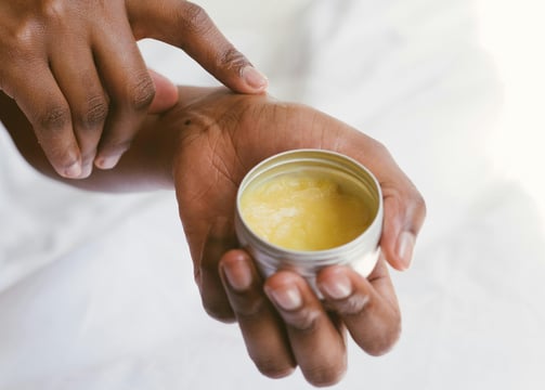 a person holding a cup of herbal salve in their hands