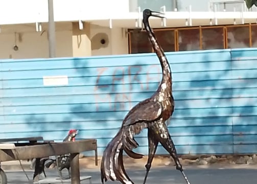 Sculpture grandeur nature d’une grue en métal recyclé, exposée sur un trottoir urbain à Dakar