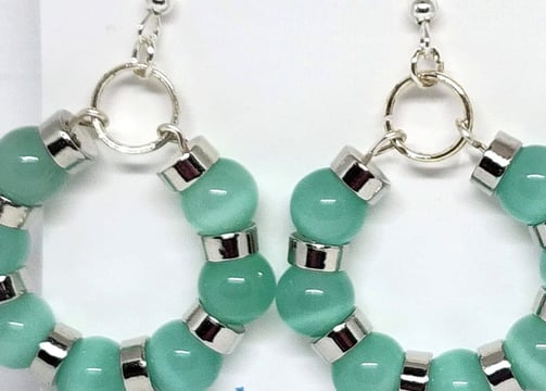 a pair of earrings with green beads and silver hoop earrings