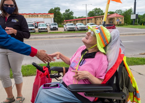 Photo of Dawn Zuterberg sitting in her electronic scooter, shaking someone's hand