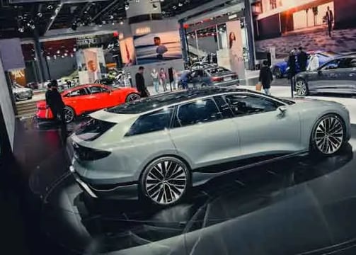 A slick, modern exhibition space featuring several high-end cars. A white sedan is prominently displ