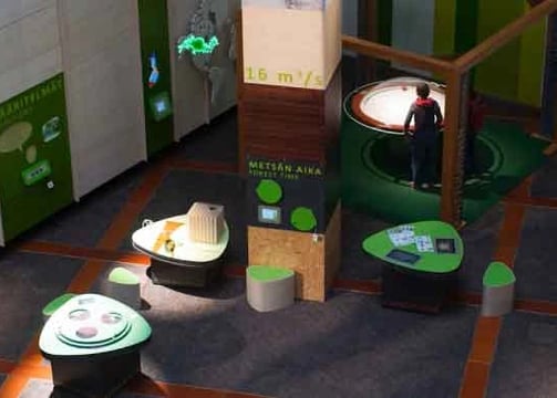 A modern exhibition space featuring interactive displays and informational panels predominantly in g