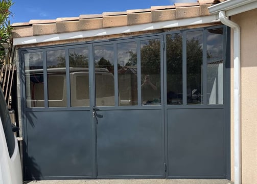 Verrière extérieure en métal gris avec porte intégrée et soubassement plein, réalisée sur mesure par un métallier ferronnier 