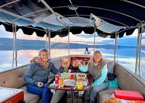 two women sitting at a table with drinks on a sunset eco-friendly electric boat cruise