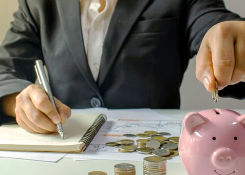 a person in a suit jacket is depositing money from one hand & holding a pen and writing on a notepad