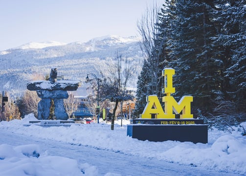 A yellow "I AM" Invictus Games sign in front of a snow-covered Whistler village 