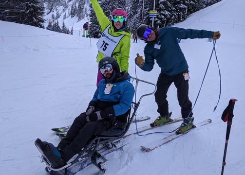 alt="Sean in his sit ski with Outdoors for All instructors Kristin and Ted, posing for the camera