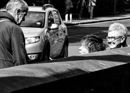 Three women, partially hidden behind a wall chat in the sunshine at Holy Corner, Edinburgh