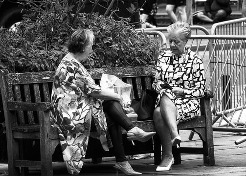 Two women sit on a bench, chatting, on a sunny day at Festival Square, Lothian Road, Edinburgh
