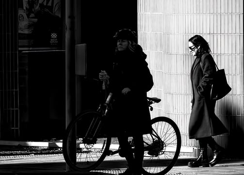 A woman on her bike, in shadow, and a woman behind her in the light at the bottom of Morningside Road, Edinburgh