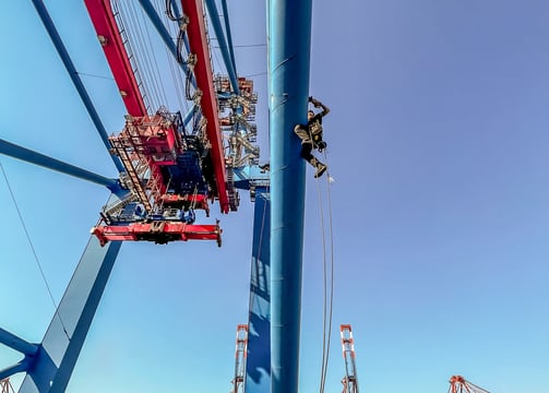 Ein Höhenarbeiter seilt sich von einem Kran am Hafen ab.