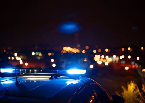 Policijos automobilio švyturėliai apšviečia naktinį miestą, simbolizuojantys saugumą ir reagavimą