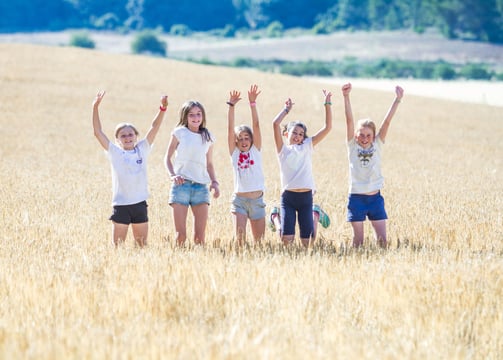 cinco niñas saltando en un campo de trigo