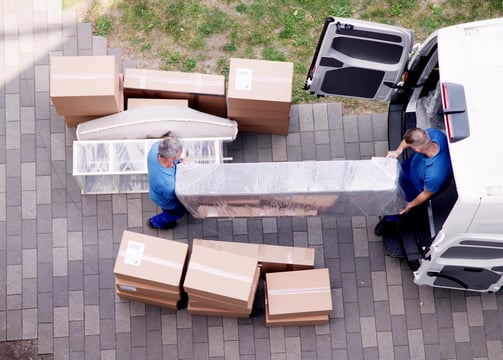 Two movers handling a wrapped specialty item and boxes during high-value delivery from van.