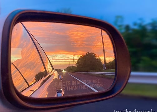 a car's side view of a car's side view mirror with bright orange sunset in it