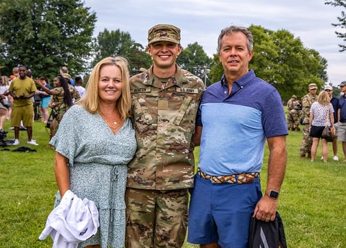 Two parents standing with their son who is in Army camoflage.  They are with other families.