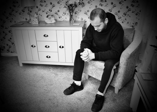 young man sat down in chair looking sad next to sideboard flowers and lamp