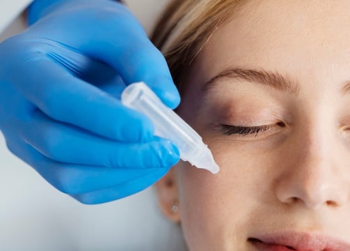 Vrouw met een chirurgisch handschoen aan dat vloeistof op een gezicht aanbrengt