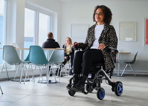 A folding powered wheelchair being used in a cafe by a happy lady enjoying a day out with her Carbon