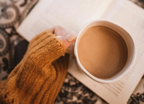 Mão feminina segurando uma xícara sobre um livro, simbolizando ancoragem suave e exploração interior