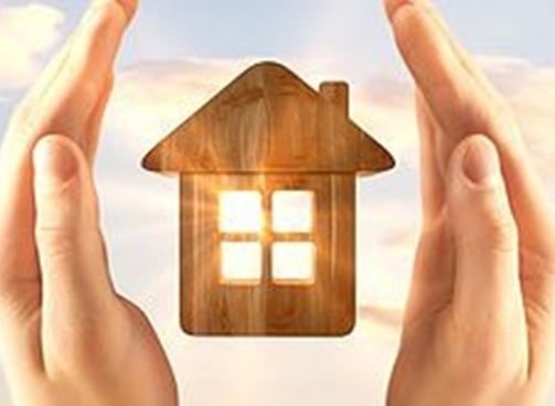 hands holding a house with a wooden house in the background