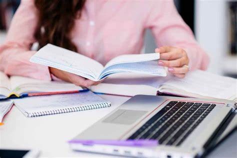 a woman is sitting at a desk with a laptop and a notebook