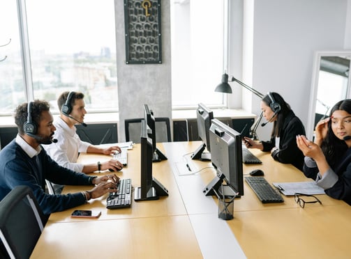Smiling customer service representative wearing a headset, sitting at a desk with a computer