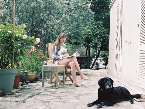 photo de l'artiste sur une chaise en train de peindre dans un jardin avec son chien