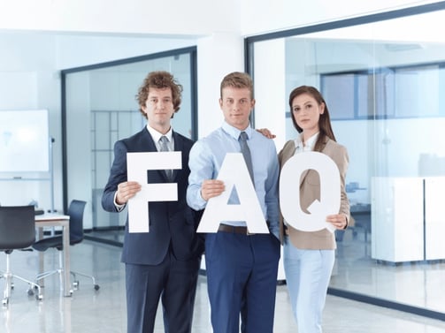 Professionals standing in an office, holding large letters 'FAQ' meaning frequently asked questions