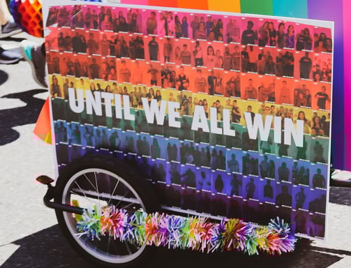 A wagon holding a rainbow sign that says "UNTIL WE ALL WIN"