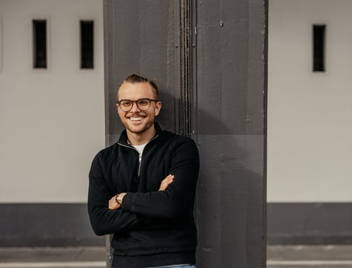 a man with glasses and a black jacket standing in front of a building