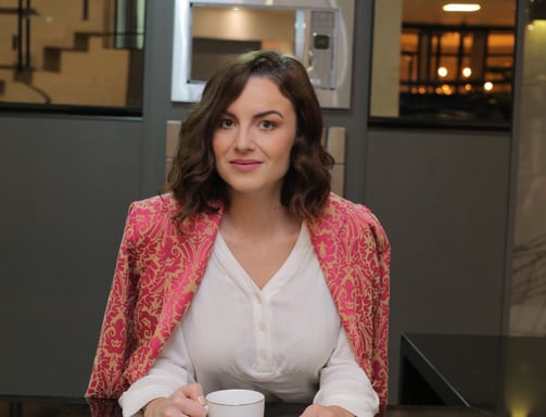 35+ woman mentor at a counter, dressed in pink and white, holding a cup of coffee