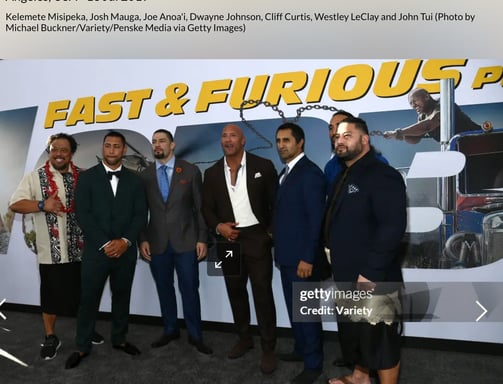 Dwayne Johnson with John Tui  in front of a fast & furious backdrop billboard 