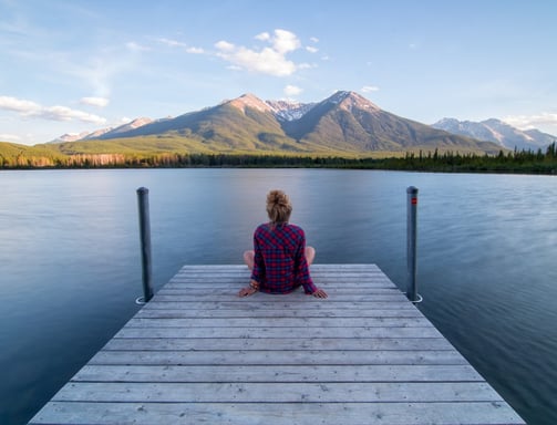 a woman sitting on a dock with mountains in the background