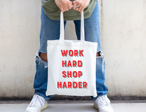 a person holding one of  work hard shop harder tote bags.