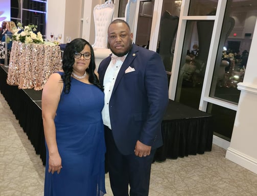 Pastor posing with his wife in suit and dress in ballroom