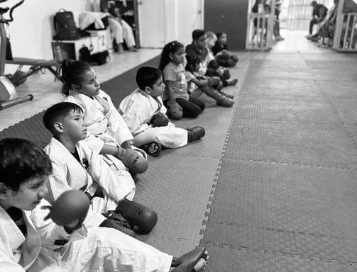 a group of kids sitting on a mat with their hands on their knees