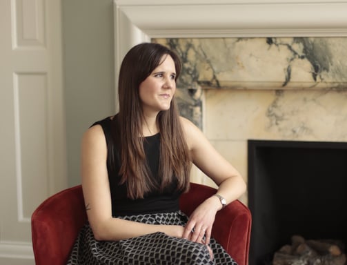 Photo of Anna Joyce expert insomnia therapist sitting in chair by marble fireplace wearing a dress