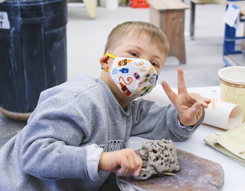 One of our youth students wearing a mask while playing with clay.